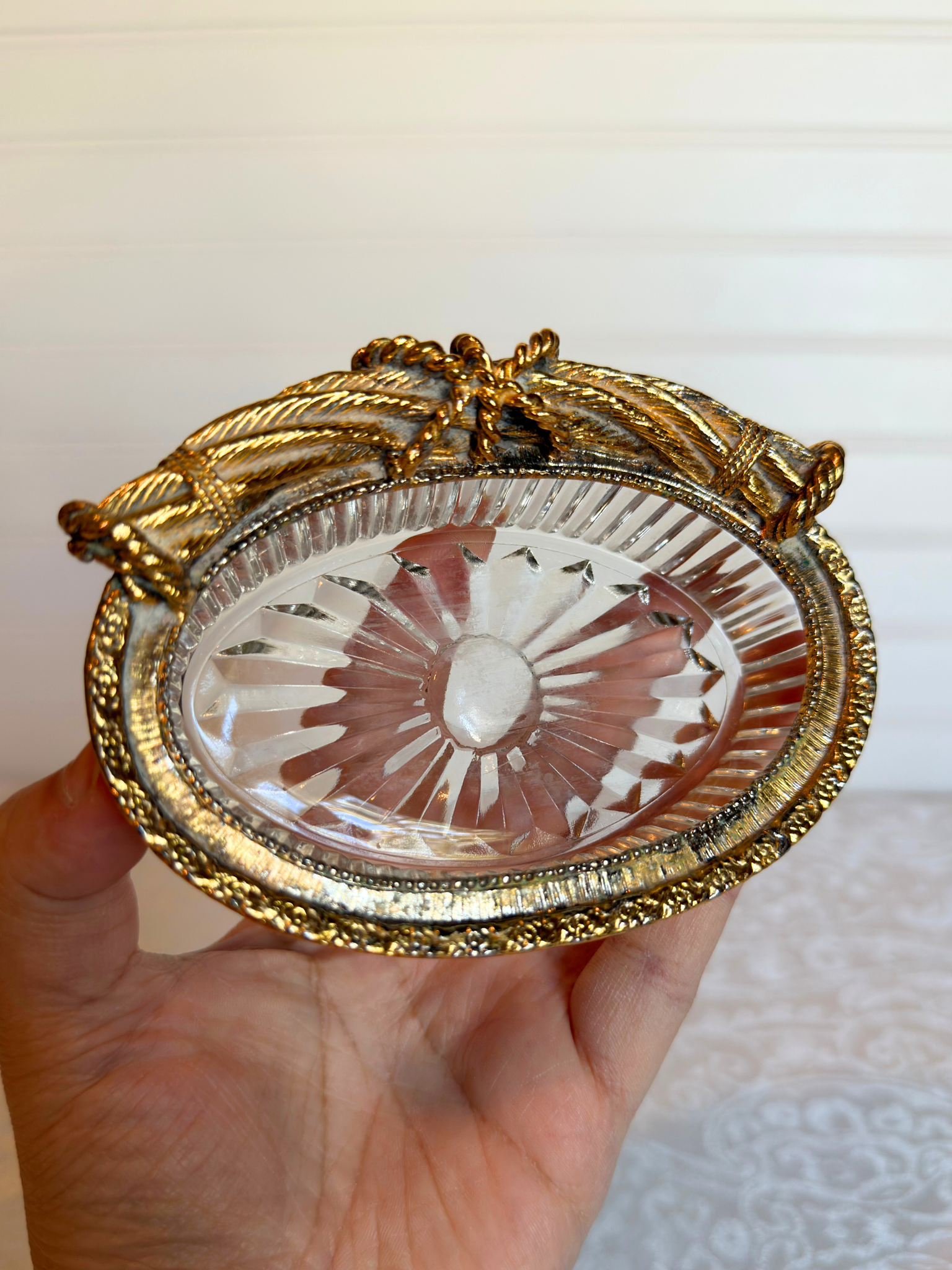 Decorative glass dish with gold rim held in a hand against a neutral background