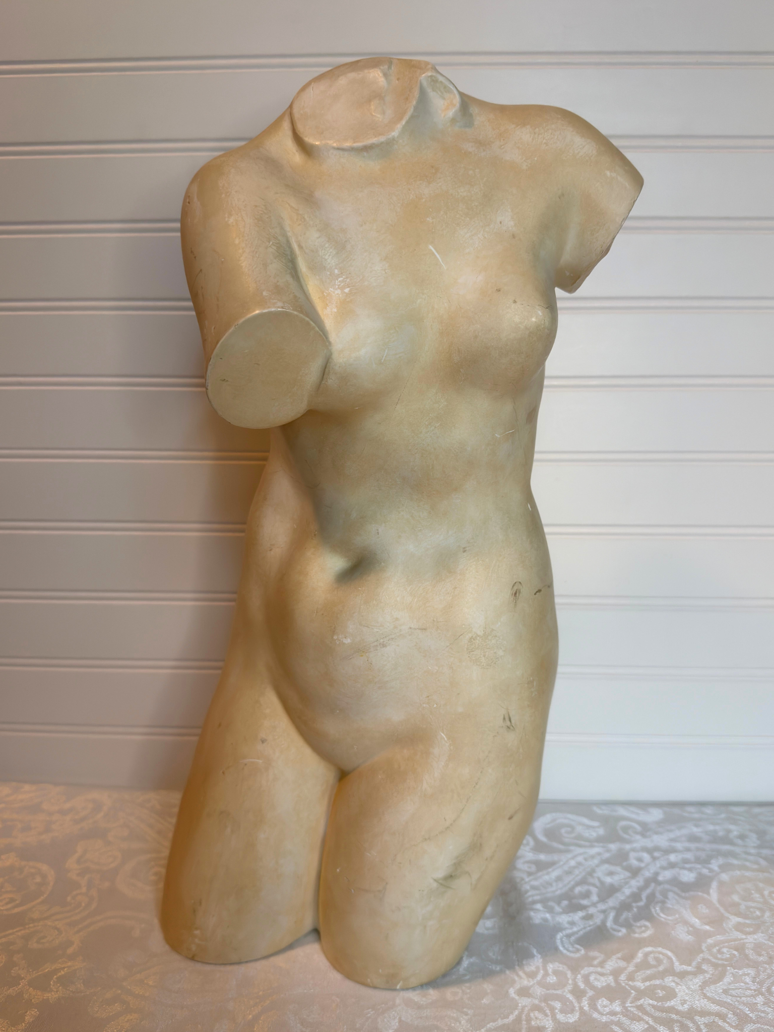 sculpture of a female torso on a textured surface with a neutral background