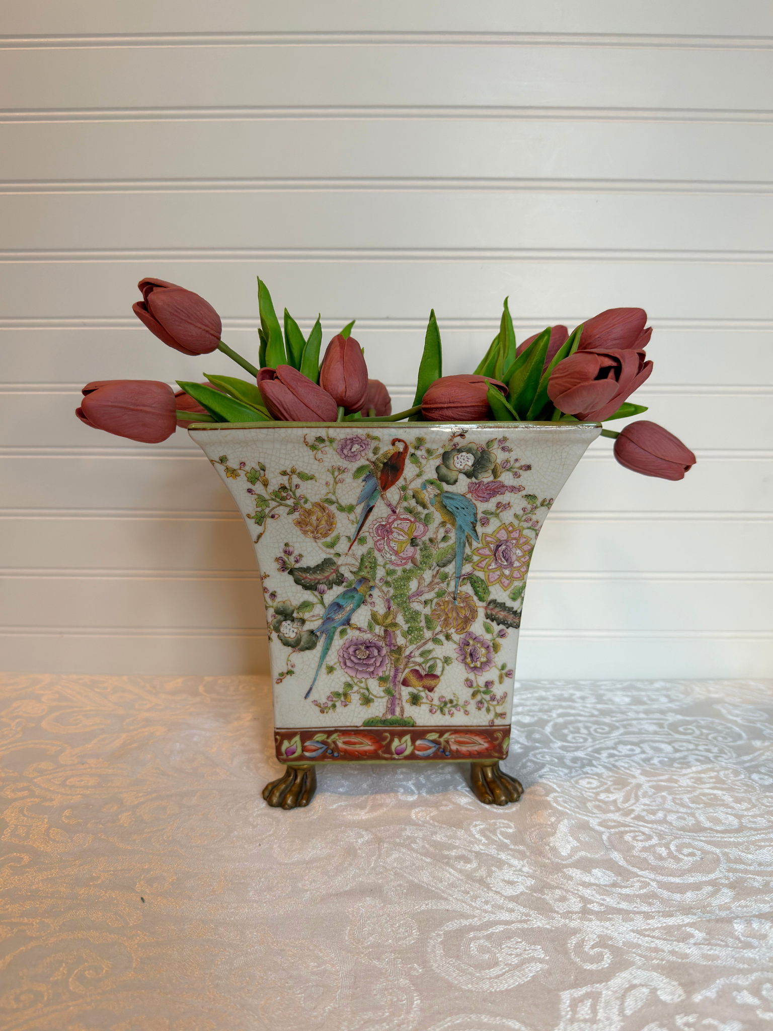 Decorative vase with floral design and bird illustrations holding pink tulips on a textured surface.