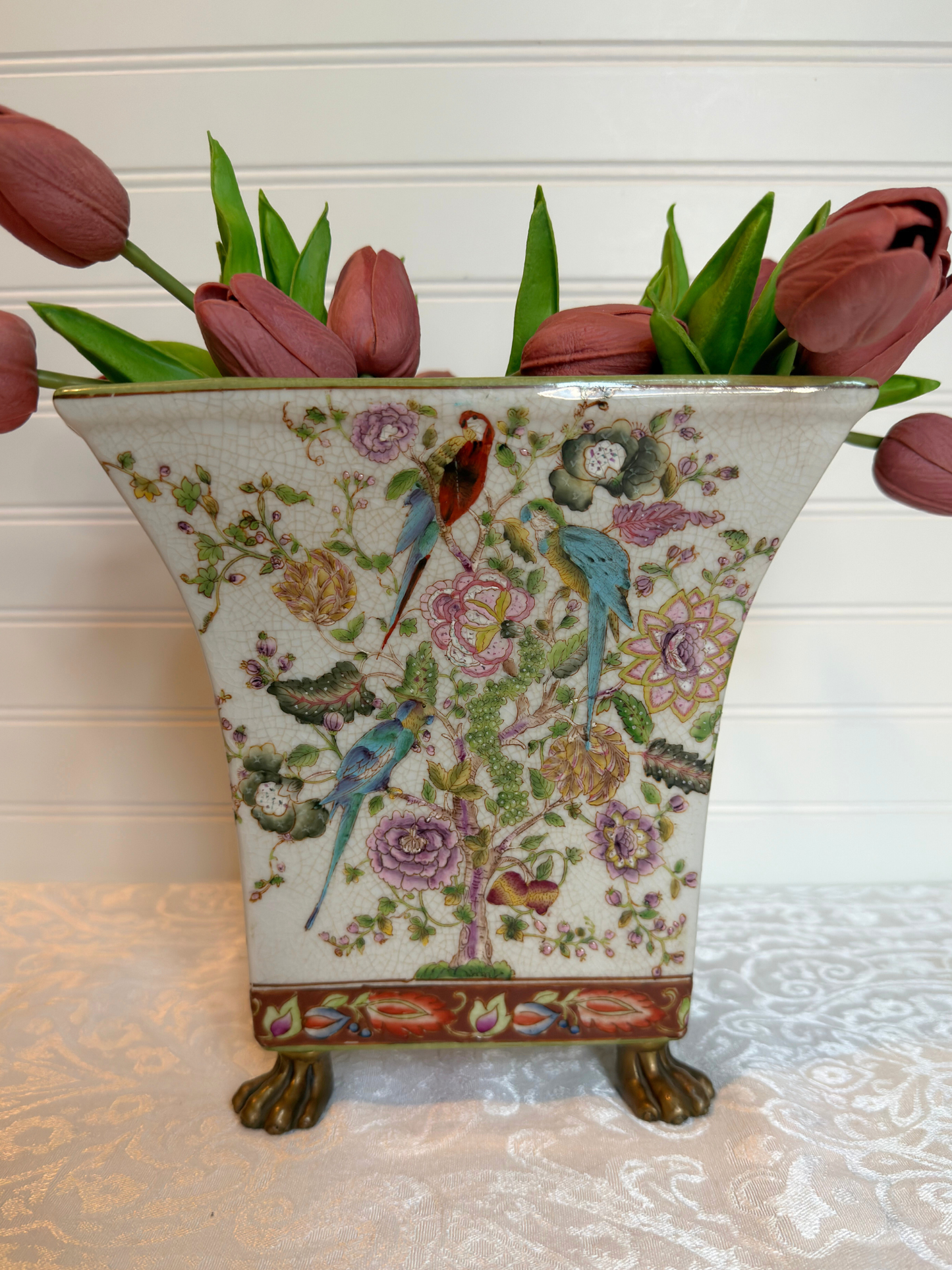 Decorative vase with floral and bird pattern holding pink tulips on a light  surface.