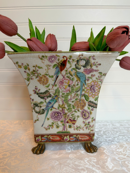 Decorative vase with floral and bird pattern holding pink tulips on a light  surface.