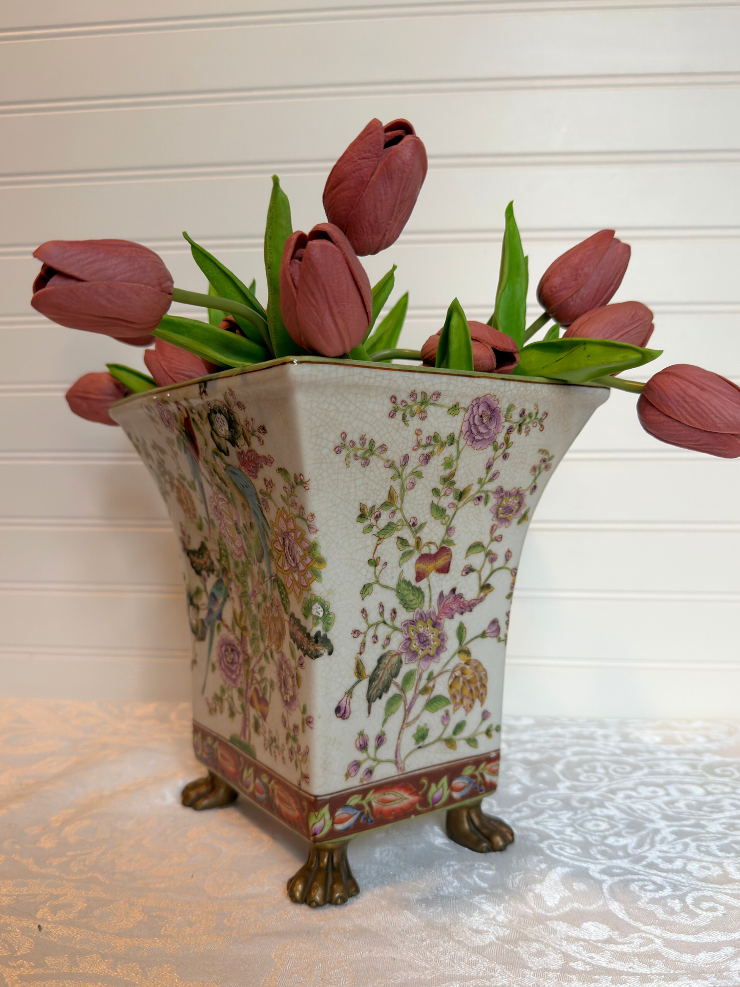Decorative vase with floral patterns holding pink tulips on a light surface.
