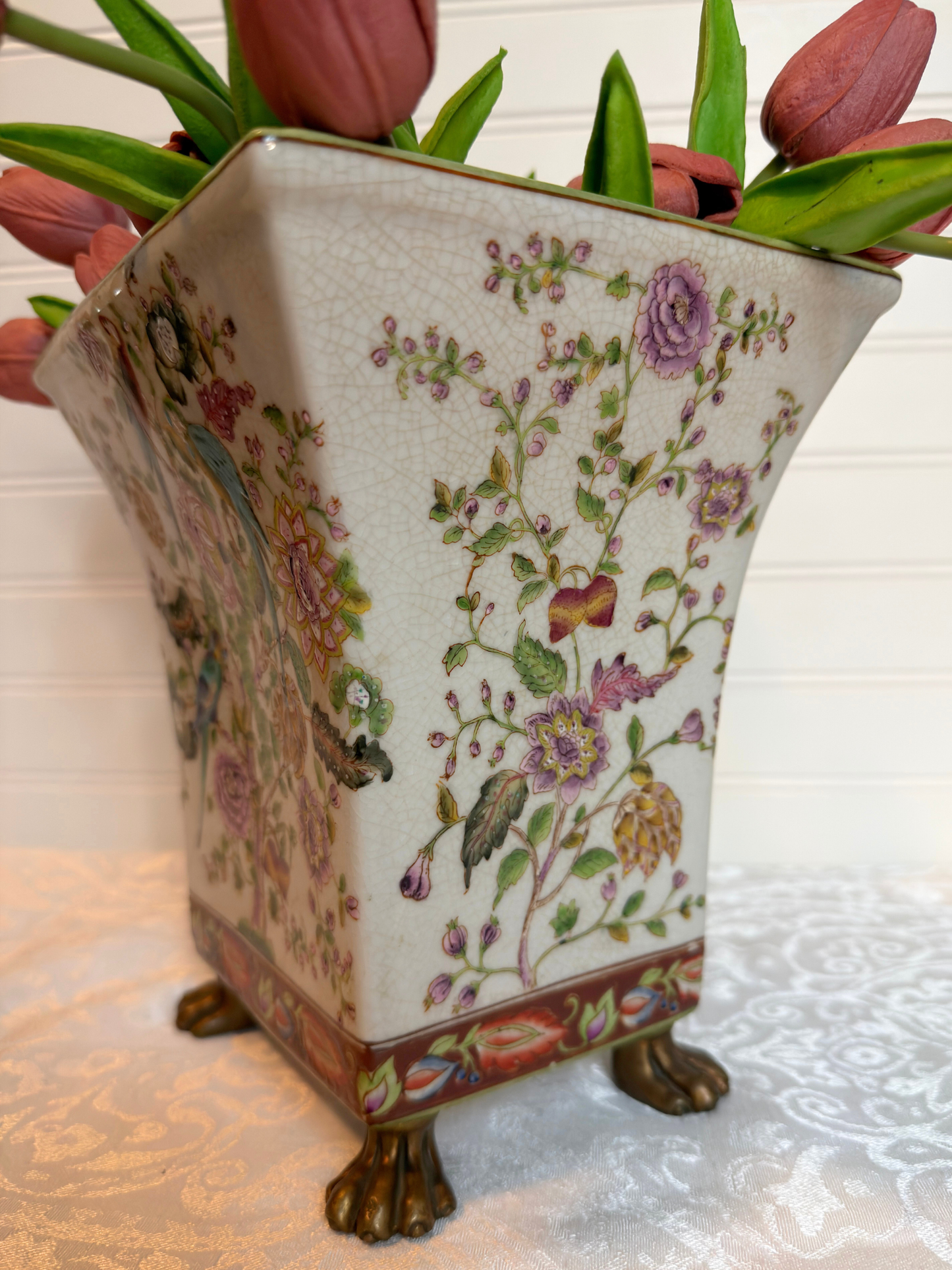 Decorative vase with floral patterns and animal figures, containing pink tulips.