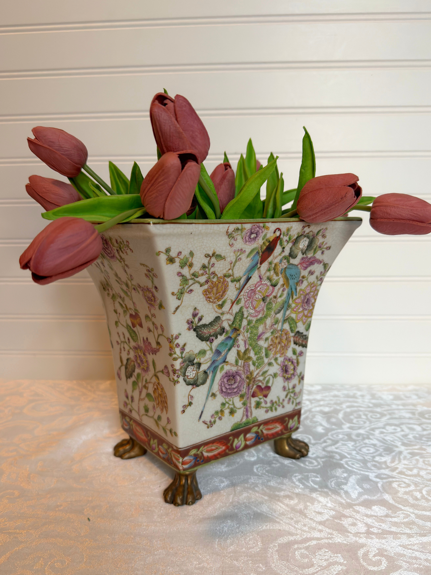 Decorative vase with floral patterns and animal figures, containing pink tulips.