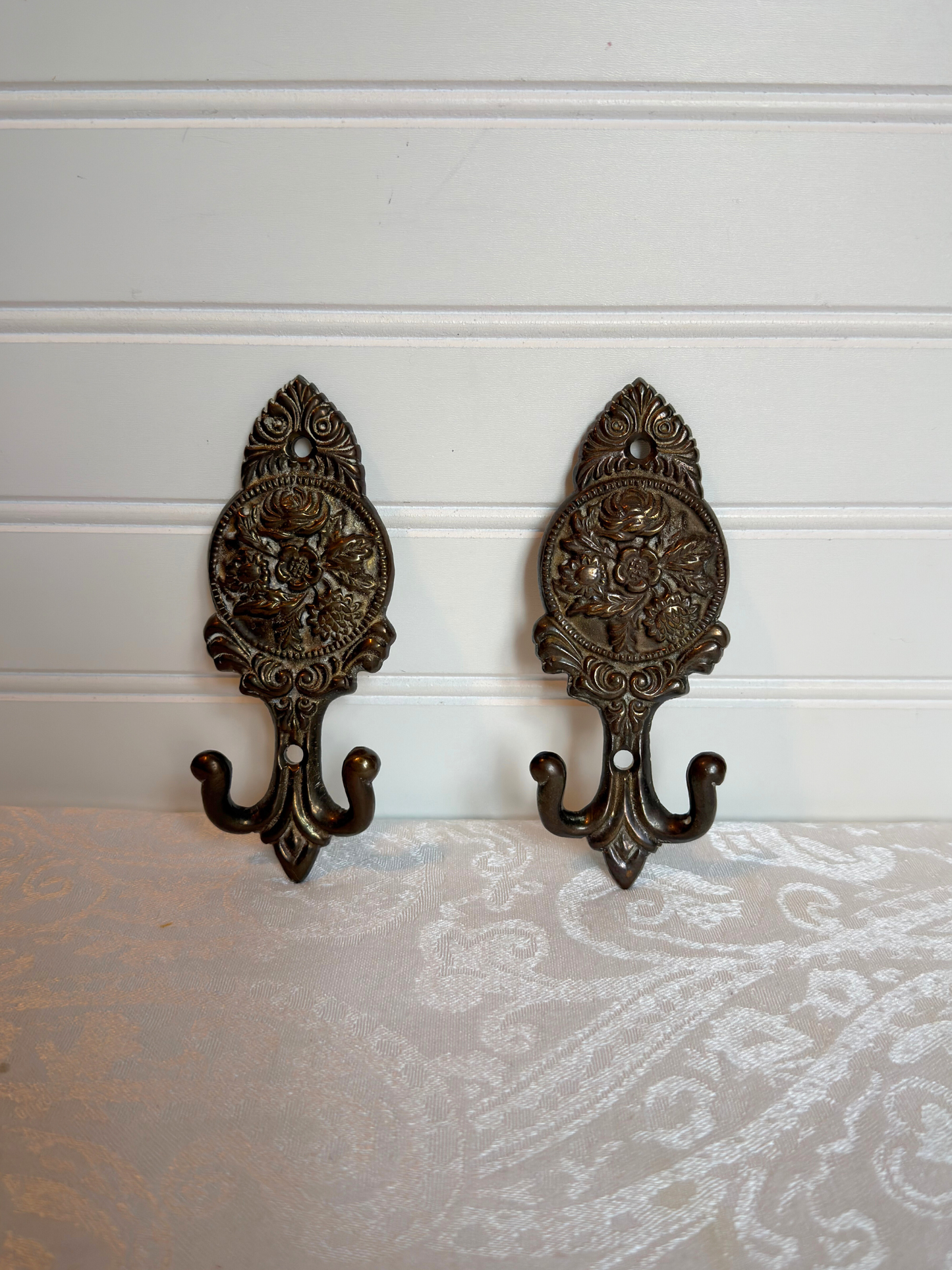 Pair of ornate brass floral wall hooks on a white background