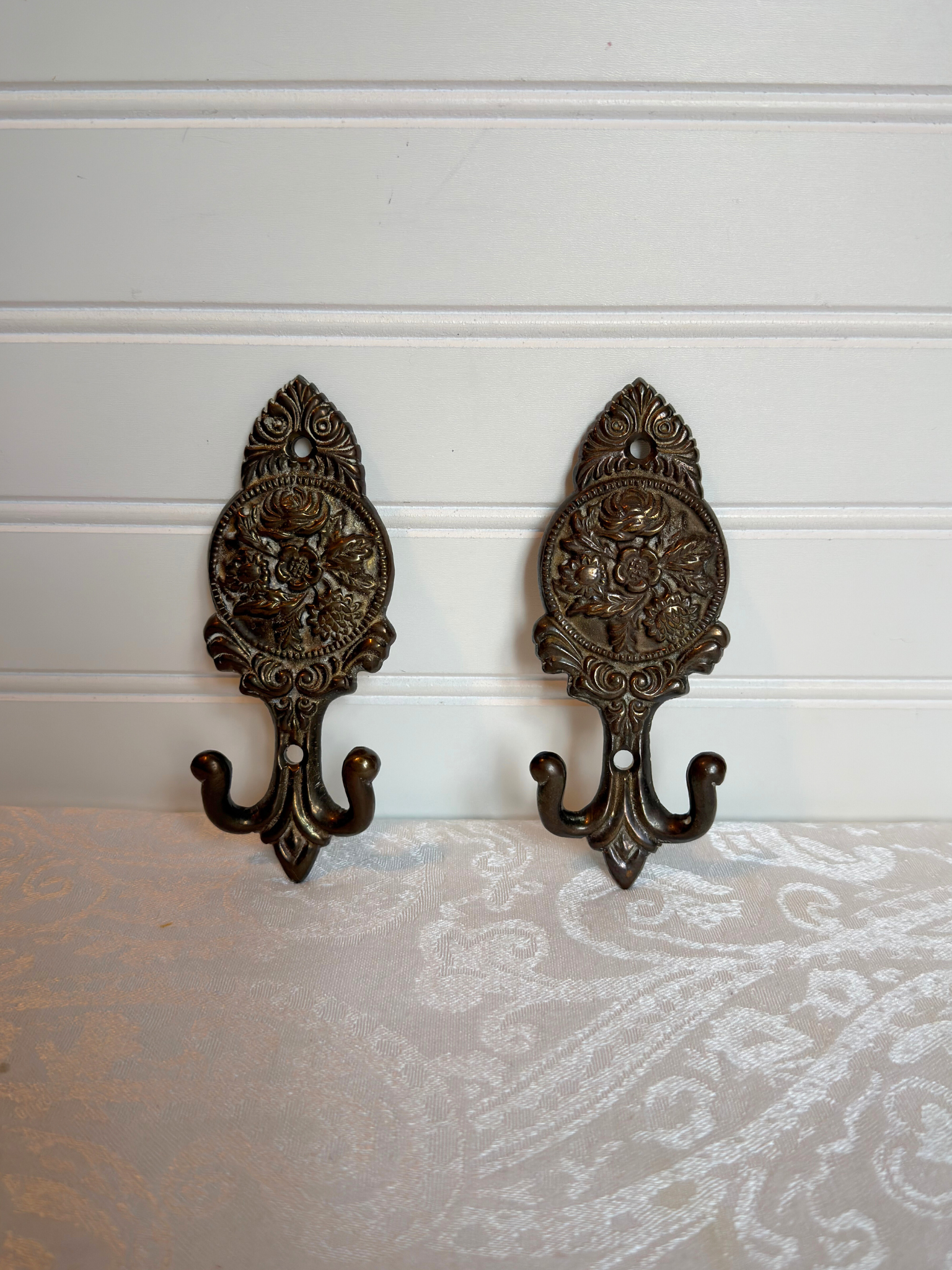 Pair of ornate brass floral wall hooks on a white background