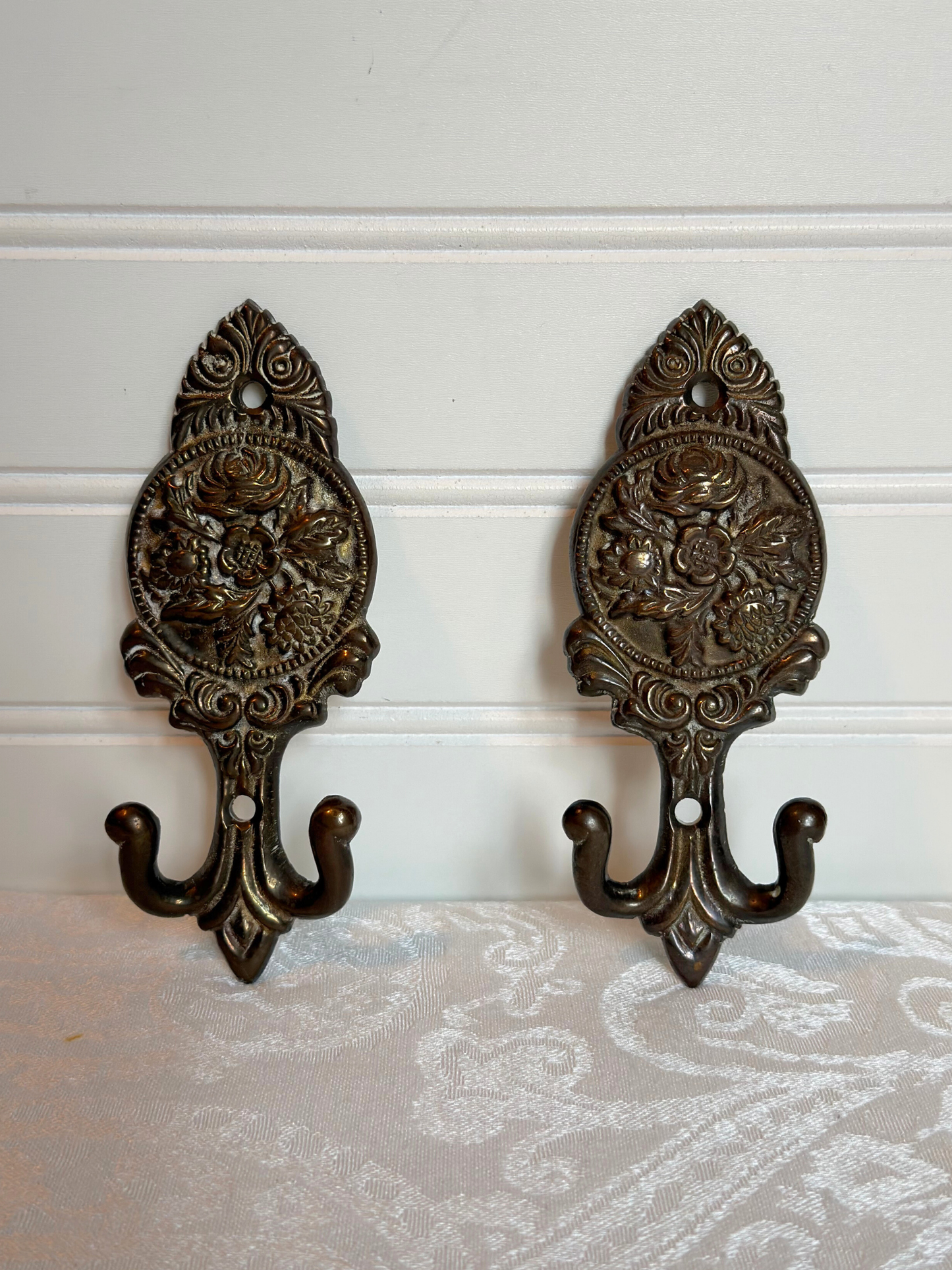 Pair of ornate brass floral wall hooks on a white background