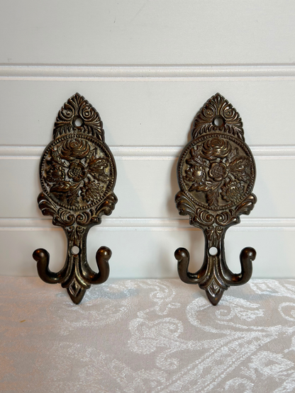 Pair of ornate brass floral wall hooks on a white background
