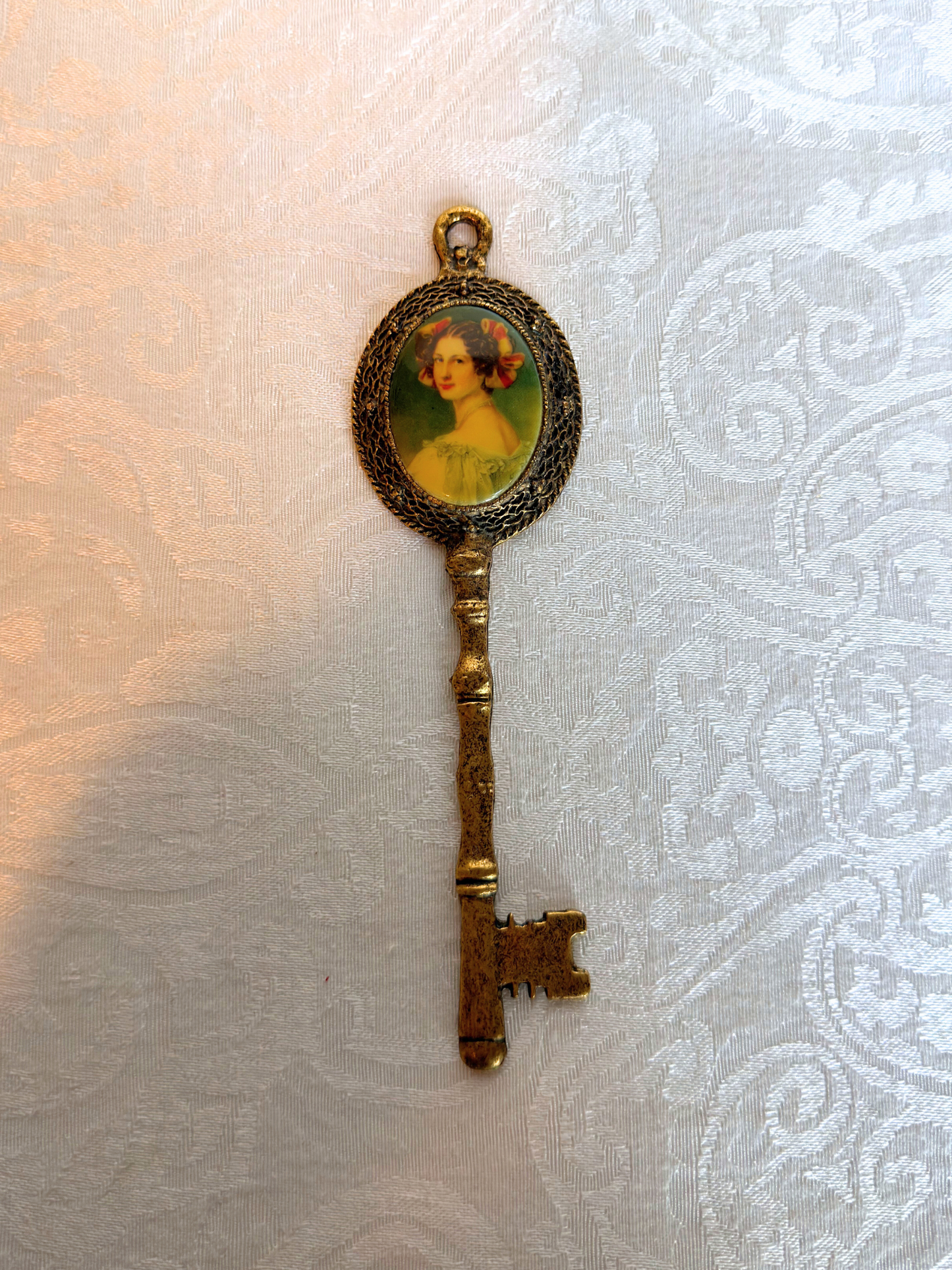 Decorative key pendant with a portrait on a textured white background