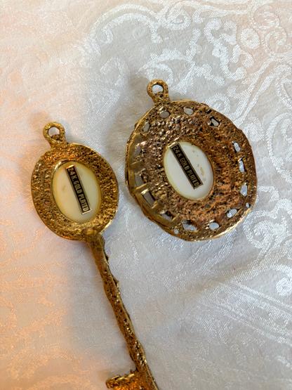back of gold pendants with intricate design on a textured white background