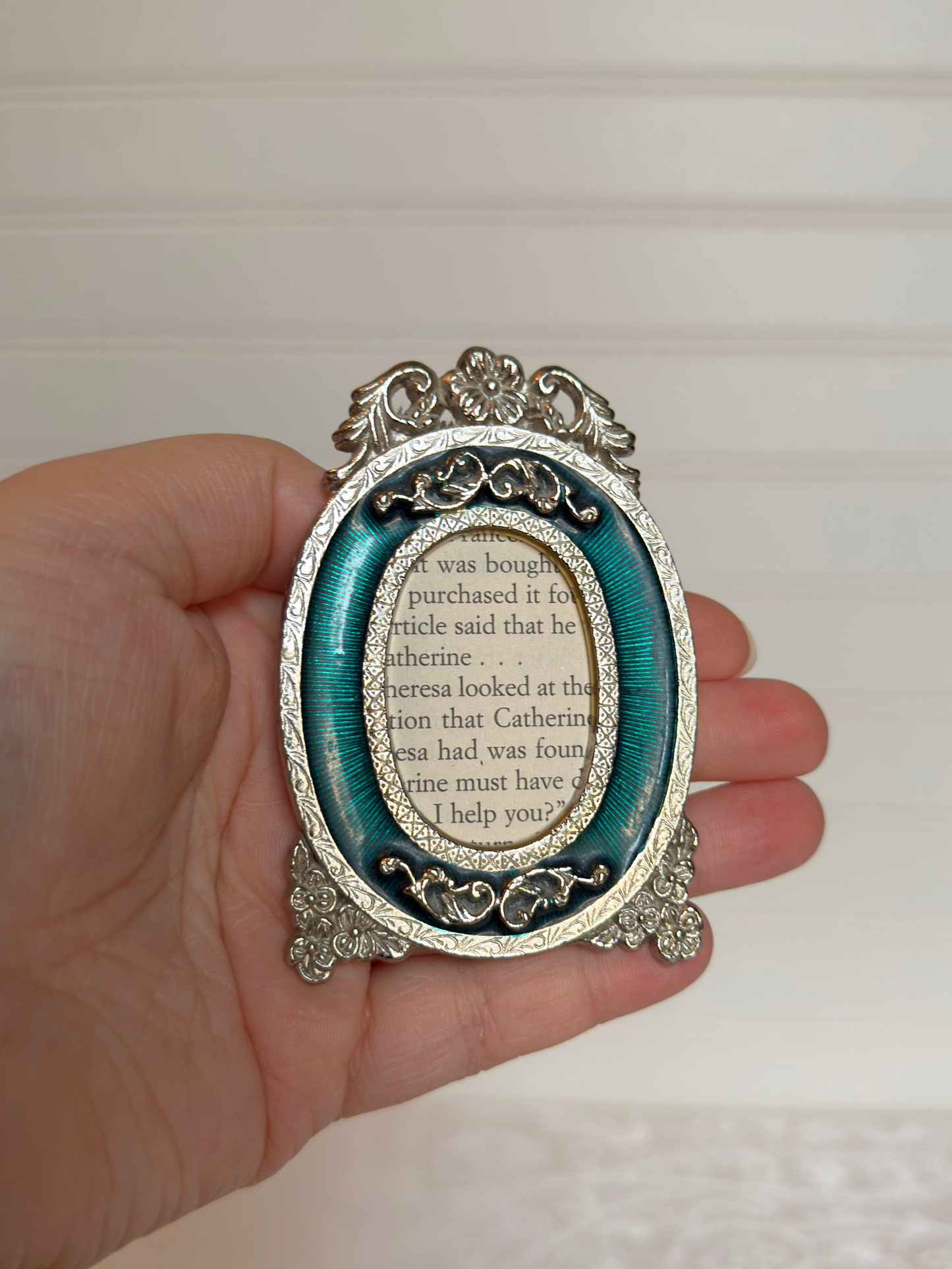 Decorative oval frame with intricate design held in a hand against a neutral background