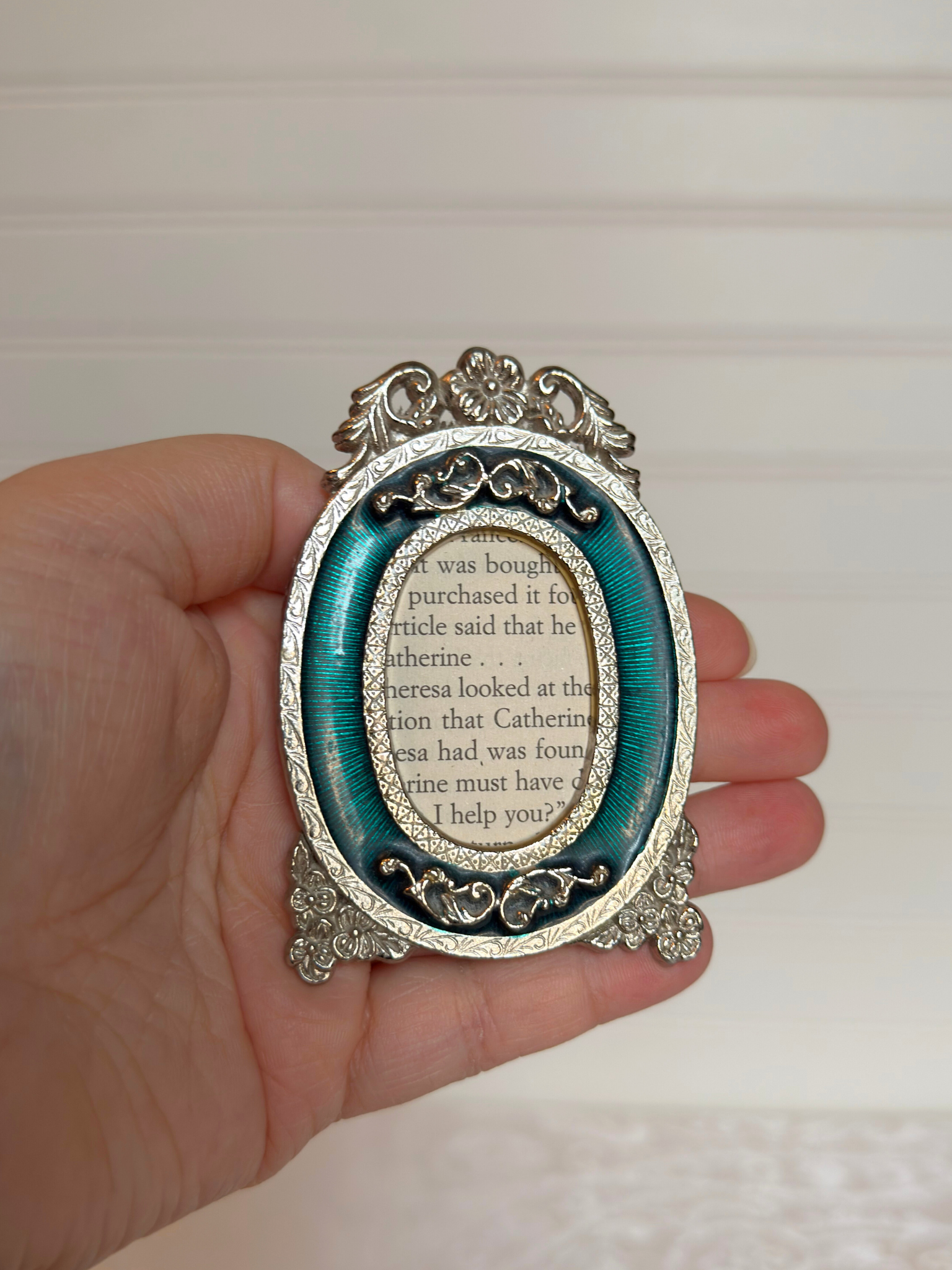 Decorative oval frame with intricate design held in a hand against a neutral background
