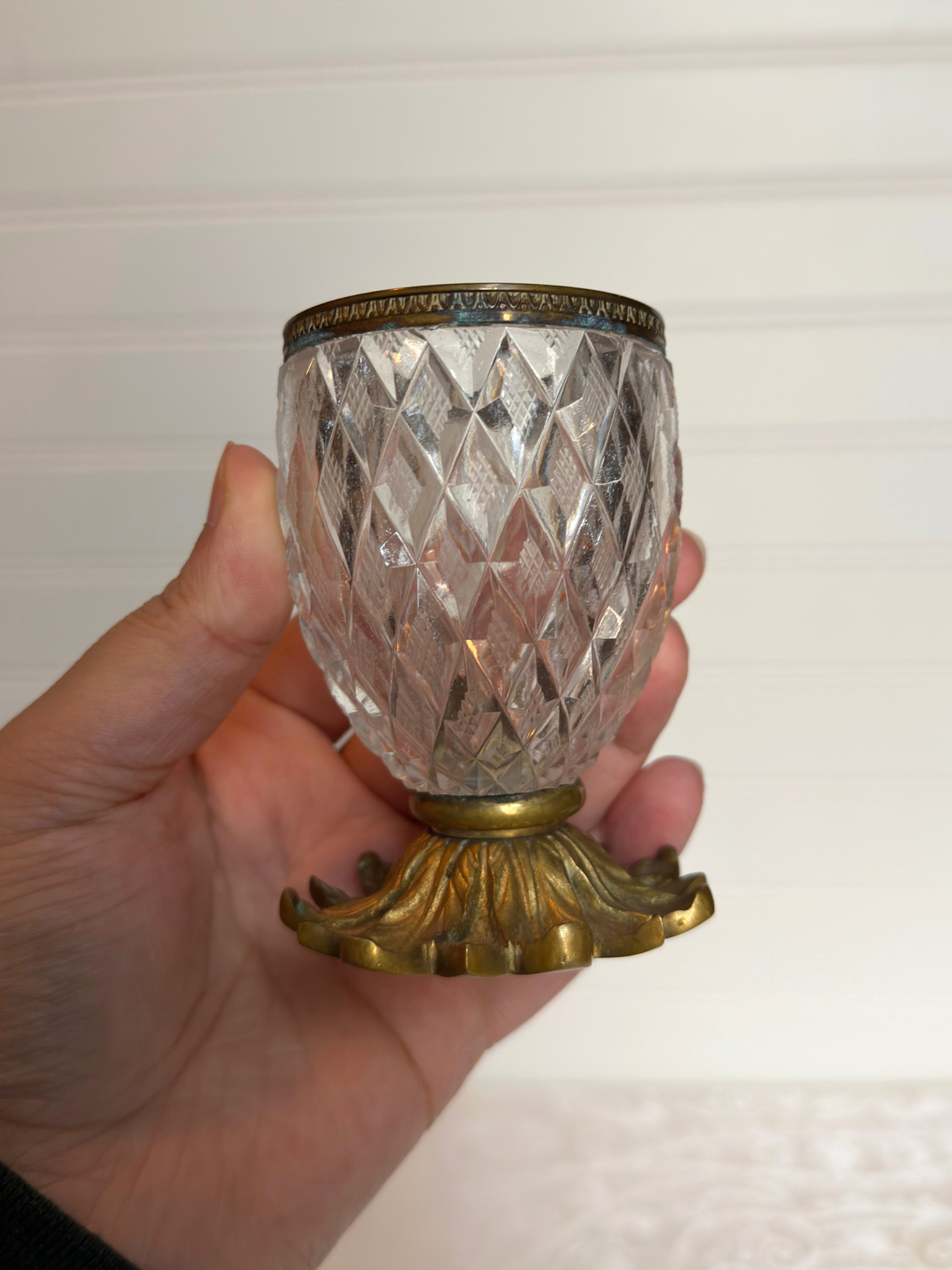 Decorative crystal holder with gold base held in a hand against a white background