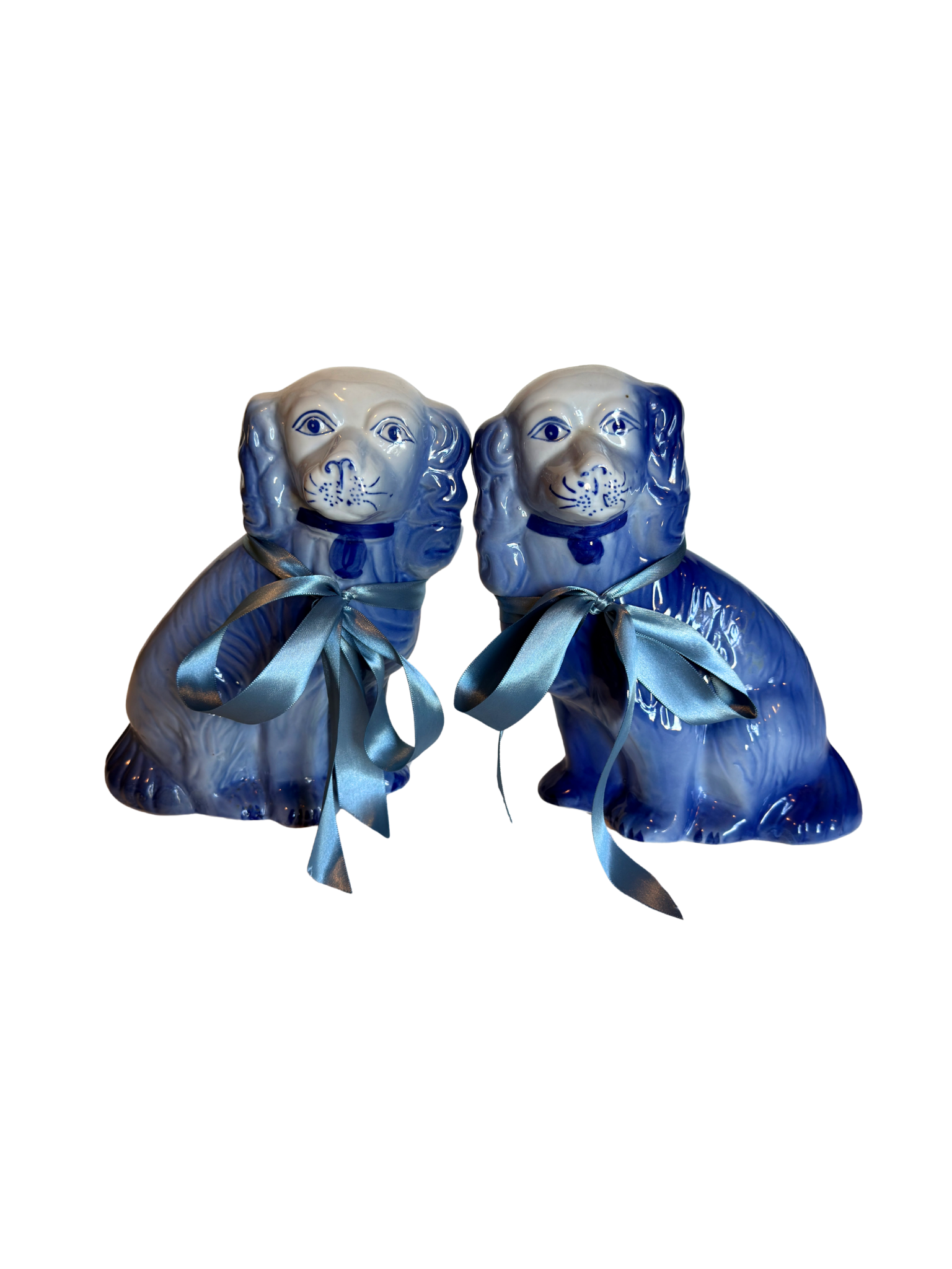 Two blue staffordshire dogs with blue ribbons on a white background