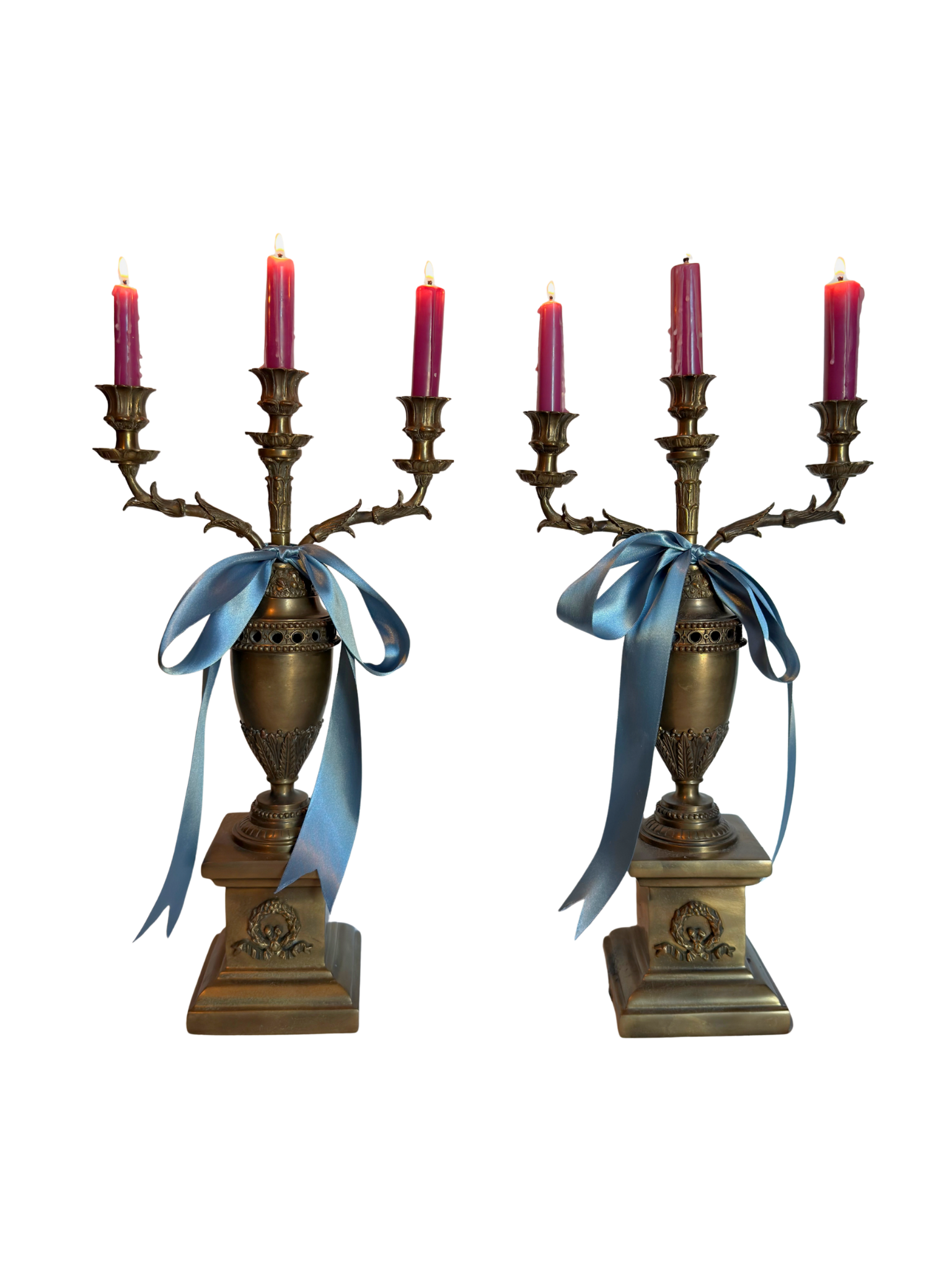 Pair of ornate brass candle holders with lit candles and blue ribbons on a white background